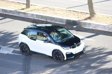 Beyaz BMW i3 elektrikli araba şehir caddesinde bir adam ve bir kadın taşıyor.