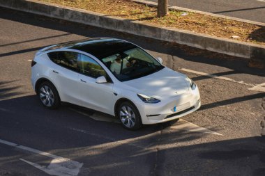 Beyaz Tesla modeli güneşli bir günde şehir caddesinde araba sürüyor.