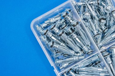 Yepyeni inşaat bağlayıcılarıyla dolu plastik organizatör kutusu mavi bir arka planda yatıyor.