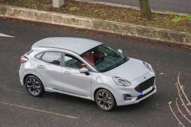Metalik gri elbiseli modern SUv ford puma, direksiyonda şoförle yolda gidiyor.