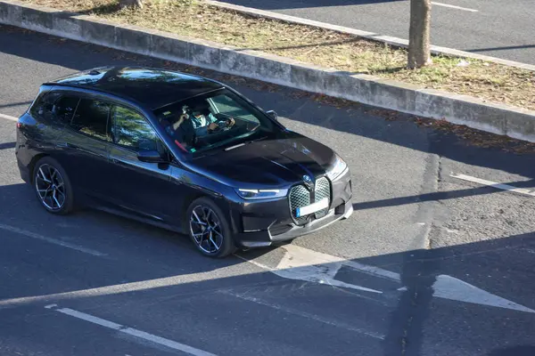 Güneşli bir günde siyah BMW ix3 elektrikli araba kullanan bir iş adamı.