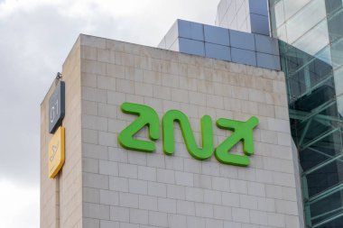 Green Anz Bankası logosu, sağı gösteren bir ok ile modern bir binanın duvarına monte edilmiş, büyümeyi ve finans alanındaki ilerlemeyi sembolize ediyor.
