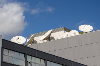Bir binanın çatısına birkaç uydu anteni yerleştirilir, mavi gökyüzüne karşı sinyaller alınır.