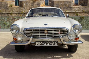 Klasik beyaz Volvo p1800 spor arabası, ikonik tasarımı ve klasik cazibesiyle park edilmiş.