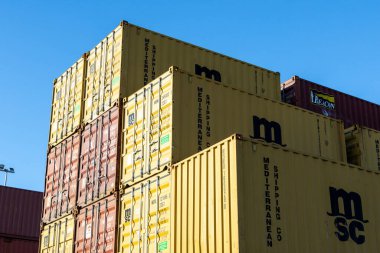 MSC Akdeniz nakliye şirketinin kargo konteynırları açık mavi gökyüzünün altındaki tersanede istiflenmiş, küresel ticaret ve lojistiği simgeliyor.