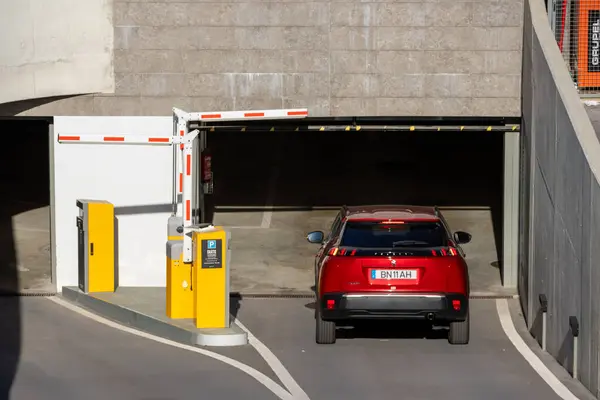 Kırmızı araba yeraltı otoparkına giriyor ödeme terminali ile birlikte açık bariyeri geçiyor.