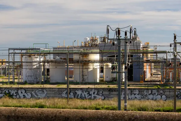 Depolama tankları, boru hatları ve elektrik hatları olan endüstriyel fabrika. Çevre duvarında grafiti olan kentsel bozulmayı gösteriyor.