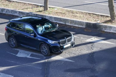 Güneşli bir günde modern siyah BMW x2 SUV kullanan bir iş adamı.