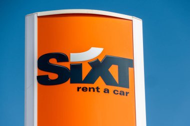 Turuncu altılı, açık mavi gökyüzünün altında şirket logosunu gösteren bir araba işareti kiralıyor.