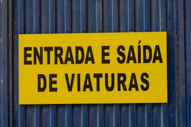 Mavi metal bir kapıya sabitlenmiş Portekizce araçların giriş ve çıkışlarını gösteren siyah harfli sarı tabela.
