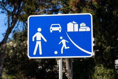 Mavi yol işareti yayayı gösteriyor, çocuk, araba ve evcilik oynuyor.