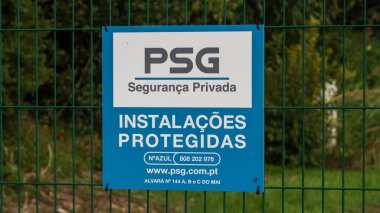 Blue psg seguranca privada sign on a green fence, indicating protected installations clipart