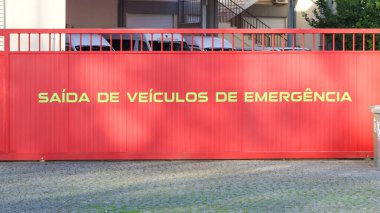 Portekiz yazısıyla kırmızı sürgülü kapı saida de veiculos de emergencia acil durum araçlarının çıkışını gösteriyor.