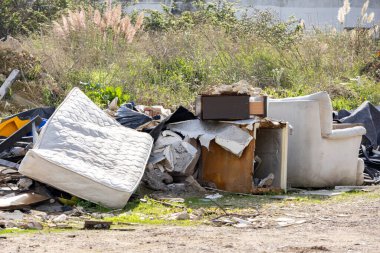 Atılmış yatak, kanepe ve mobilyalar bir tarlaya atılmış. Çevre kirliliği ve yasadışı atık tasfiyesini gösteriyor.