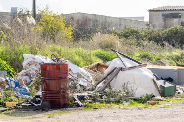 Atılmış inşaat malzemeleri ve kırmızı fıçı çevresel kirliliği ve yasadışı boşaltmayı gösteriyor.