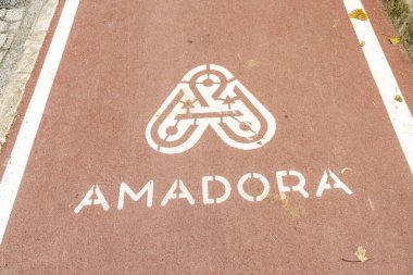 Portekiz, Amadora şehrinin logosuna sahip bisiklet yolu tabelası, şehir manzarasında gezinen bisikletçilere net bir yön sağlar.
