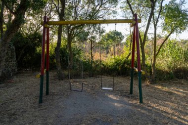 Güneşli bir yaz gününde ıssız bir parkta salıncakta sallanan iki boş salıncak.