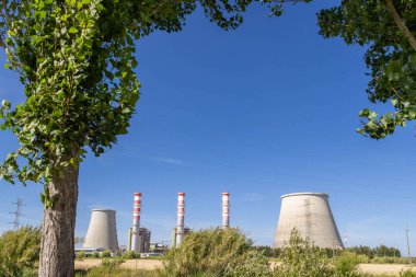 Ribatejo elektrik santrali bacaları ve soğuk kuleler açık mavi gökyüzünün altında Portekiz kırsalının üzerinde yükseliyor.