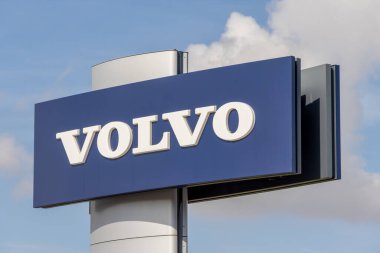 Volvo logosu mavi gökyüzünde bulutlu bir direğin üzerinde sergilenir.