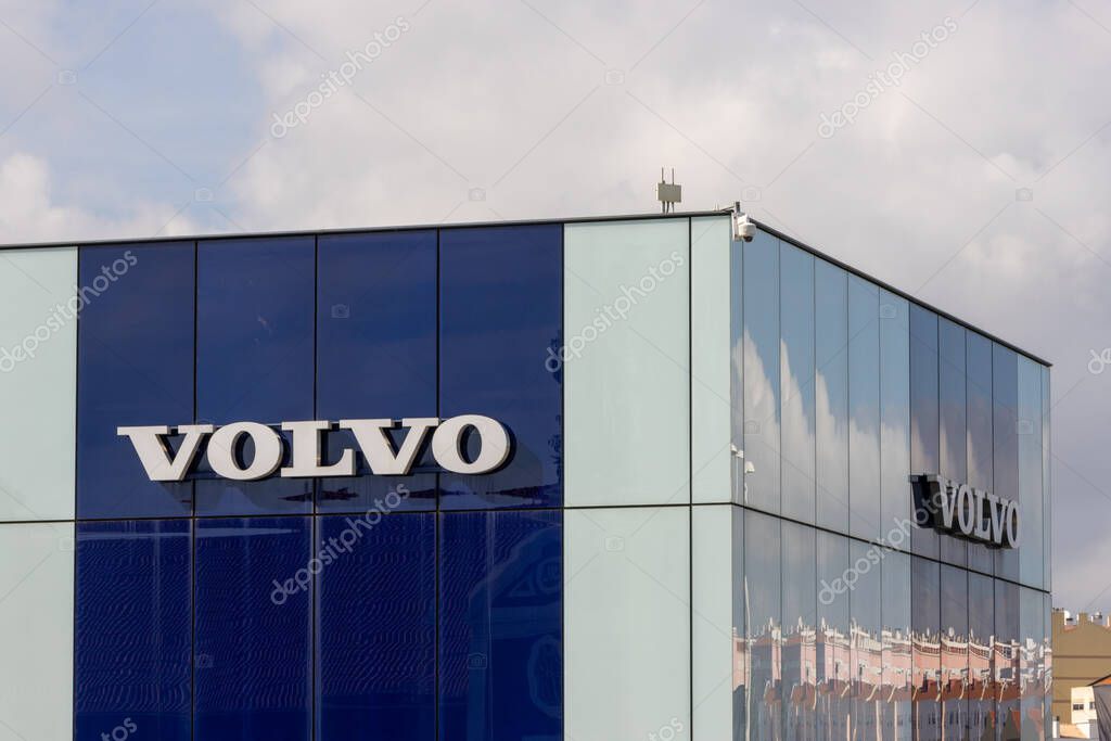 Volvo logo displayed on a modern glass building, reflecting the cloudy sky above