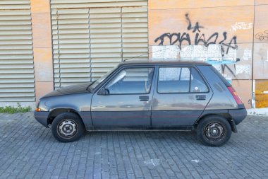 Gri renault 5 gtl duvar yazısı ve posterlerle dolu duvarın yanındaki tuğla kaldırıma park edilmiş.