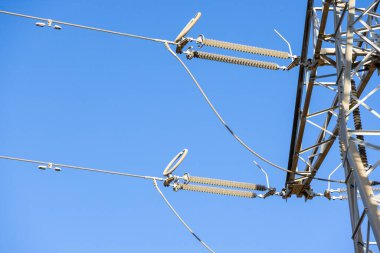 Yüksek voltaj hatları ve açık mavi gökyüzüne karşı seramik yalıtımlı güç dağıtım altyapısı