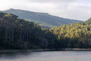 Sintra, Portekiz 'deki rio da mula barajı arka planda yemyeşil yapraklar ve dağlarla güneş ışığını yansıtıyor.