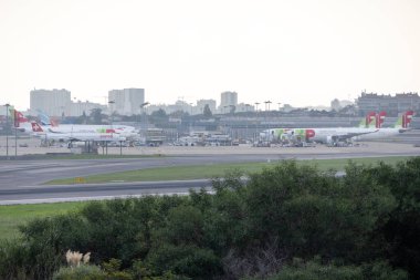 Lizbon havaalanının önüne park etmiş birkaç uçak var. Arka planda şehrin silüeti var.