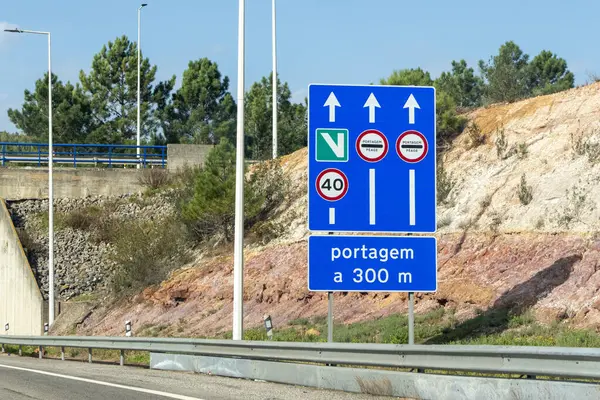 Hız limitini gösteren mavi yol işareti, verde elektronik geçiş ücreti, düzenli geçiş ücreti, ve 300 metre ilerideki gişe kapısı.