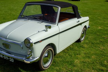 Klasik beyaz otobianchi bianchina Cabriolet üstü siyah üstü açık yeşil çimen tarlasına park edilmiş.