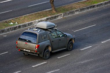 Dark gray mitsubishi l200 triton pickup truck driving on an asphalt road with a roof box clipart