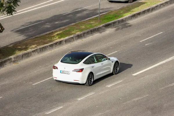 Beyaz Tesla modeli 3 elektrikli araba şehir ortamında otoyolda gidiyor, sürdürülebilir ulaşım sergiliyor