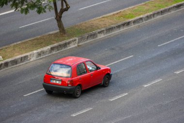 Red nissan micra driving on asphalt road near green grass and tree clipart