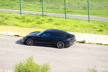 Lüks elektrikli araba Porsche Taycan yarış pistinde çimlerin yanında sürüyor.