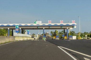 Güneşli bir günde boş otoyol gişeleri ve açık şeritleri gösteren yeşil trafik ışıkları.