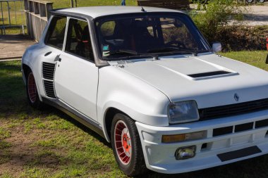 Klasik beyaz renault 5 turbo rali arabası çimlerin üzerine park edilmiş, ikonik tasarımı ve motor sporu mirası sergileniyor.