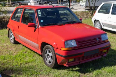 Klasik kırmızı renault 5 gt turbo çimenli bir alana park edip güneşli bir günün tadını çıkarıyor.