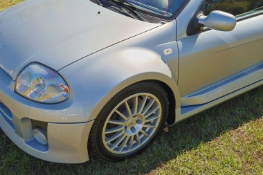 Çimenli bir araziye park edilmiş gümüş renault klio v6 spor, spor tasarımı ve alaşım tekerlekleri sergileniyor.