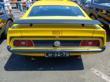 Sarı bir Ford Mustang Mach 1 'in arka görüntüsü park edilmiş, spoiler ve stop lambalarını gösteriyor.