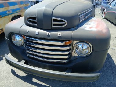 Eski bir Ford F serisi pikap kamyonetine yakın, yenilenmiş krom ızgarasını, farını ve yıpranmış vücudunu bir araba fuarında parkediyor.