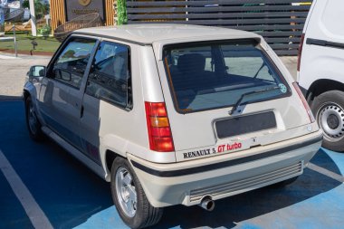 Rear view of a white renault 5 gt turbo parked on blue asphalt, showcasing its classic design clipart