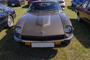 Klasik bir araba toplantısı sırasında çimlerin üzerine park edilmiş kahverengi bir Datsun 240 z 'ın ön görüntüsü.