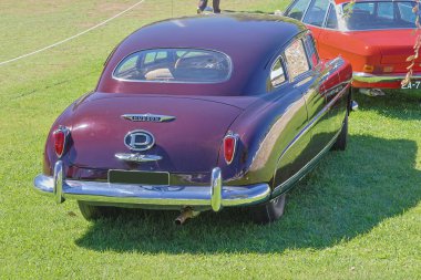 Klasik Hudson Commodore arabası çimenli bir alana park edilmiş, klasik tasarımı ve krom detaylarıyla sergileniyor.