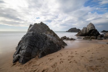 Praia da Adraga sahilindeki kumları işaret eden ayak izleri sintra, Portekiz 'de, heybetli kayalar ve dramatik bir bulut manzarası ile sakin ve büyüleyici bir manzara yaratıyor.