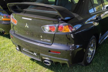 Siyah Mitsubishi Lancer Evrimi 'nin arka görüntüsü çimenlerin üzerine park edilmiş, spoiler, stop lambaları ve egzoz borularını gösteriyor.