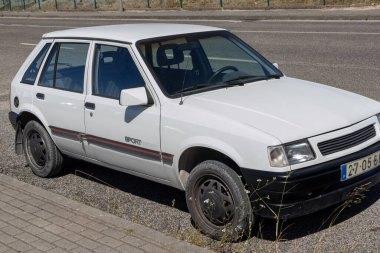 Beyaz Opel Corsa 1.2l yol kenarına park etmiş, yaş ve giysi belirtileri gösteriyor.