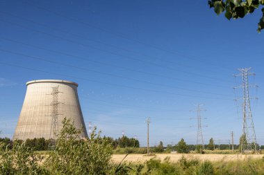 Portekiz 'deki Ribatejo termoelektrik santralinin büyük soğutma kulesi ve elektrik direkleri açık mavi gökyüzünün altında.