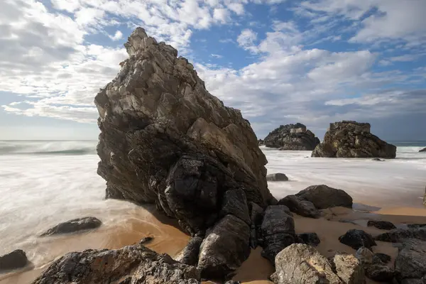 Sintra, Portekiz 'deki Adraga Sahili' nin köpüklü sulardan çıkan taşlı uzun pozlu fotoğrafı.