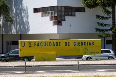 Sarı beton tabela, arka planda modern mimari yapısıyla Lizbon, Portekiz Üniversitesi Bilim Fakültesini gösteriyor.