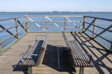 Tahta banklar, güneşli bir günde huzurlu manzaralar sunan sakin bir göle bakan bir rıhtımda dinlenme yeri sağlar.